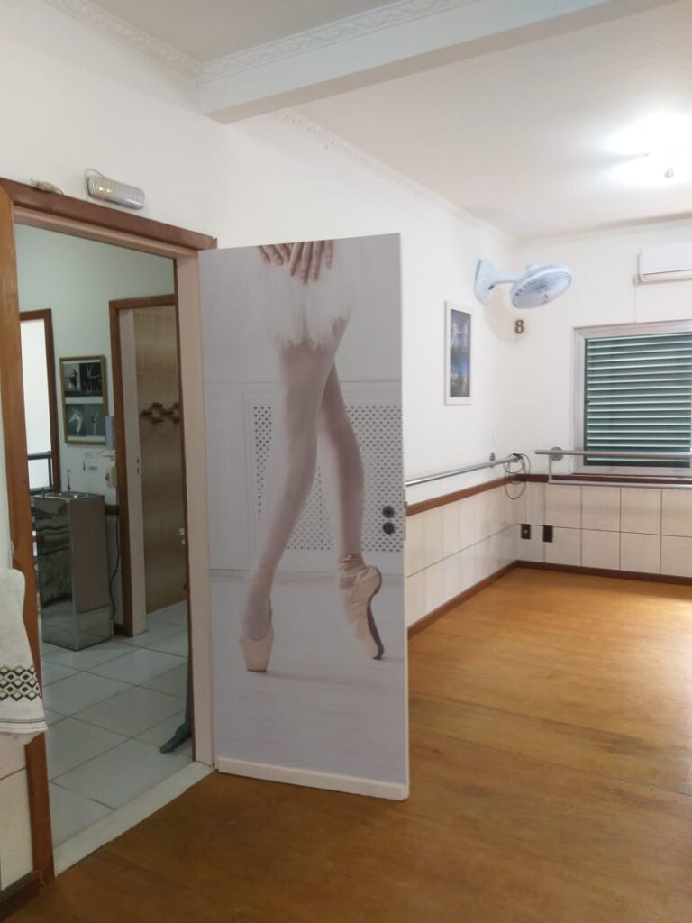 Imagem da porta da sala principal, com a imagem de uma perna com sapatilha de ponta